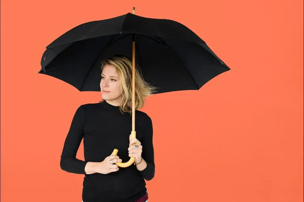 Pessoa segurando um guarda-chuva personalizado elegante em um dia chuvoso na cidade, com reflexos no chão molhado.