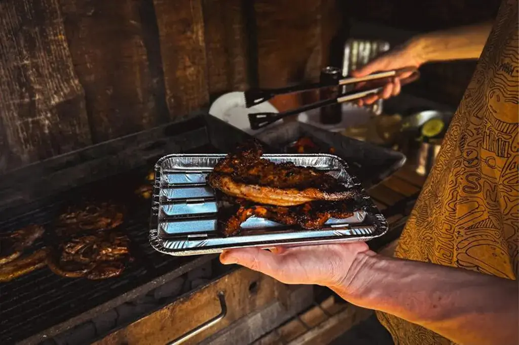 Estojo de kit churrasco personalizado com facas e garfos de aço inox com gravação de logotipo, dispostos sobre uma tábua de rústica de madeira.